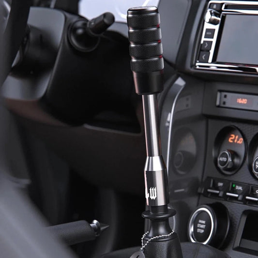 Close-up of a car gear shift lever with a detailed design, set against the interior of a vehicle.